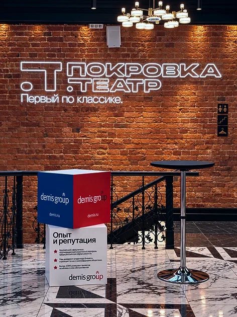 Неоновая вывеска «Покровка.Театр» на кирпичной стене и куб Demis Group в фойе