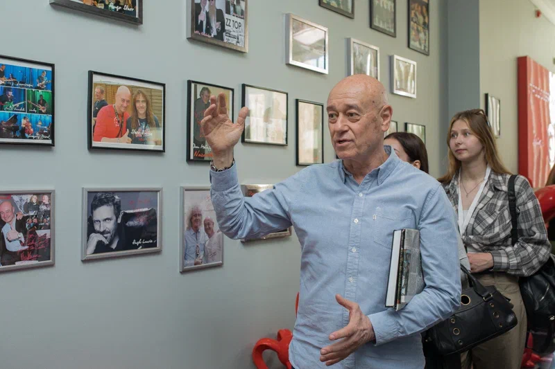 Мужчина показывает жестом на стену с фотографиями артистов